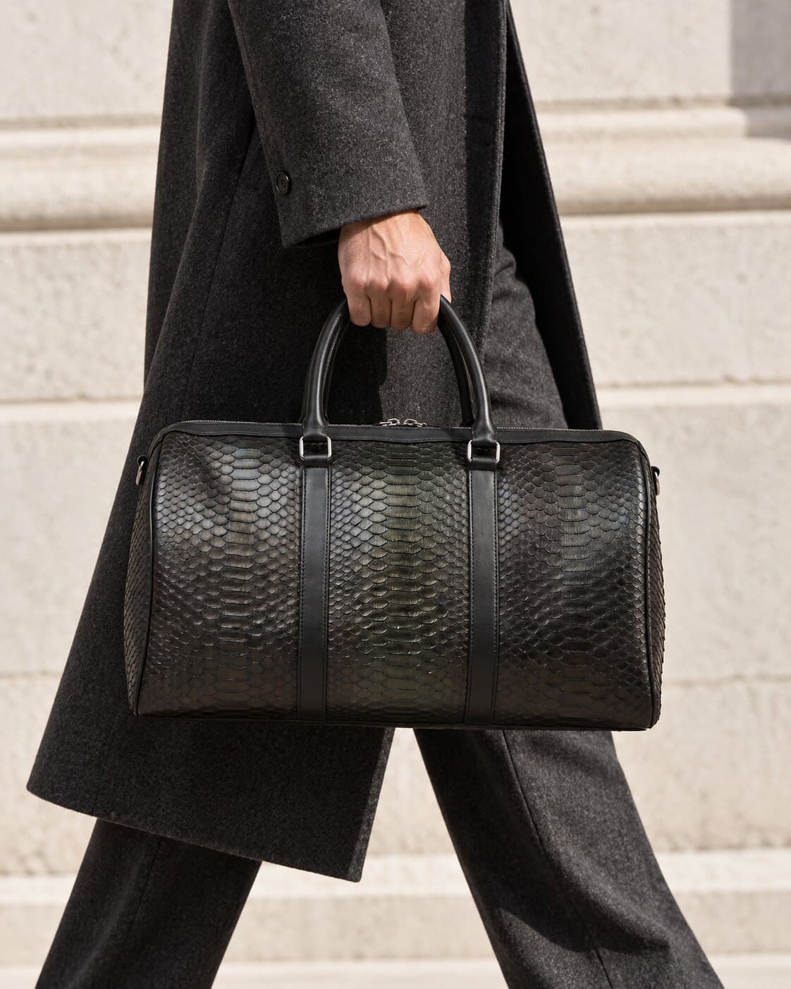 A person in a dark coat carrying a black python bag