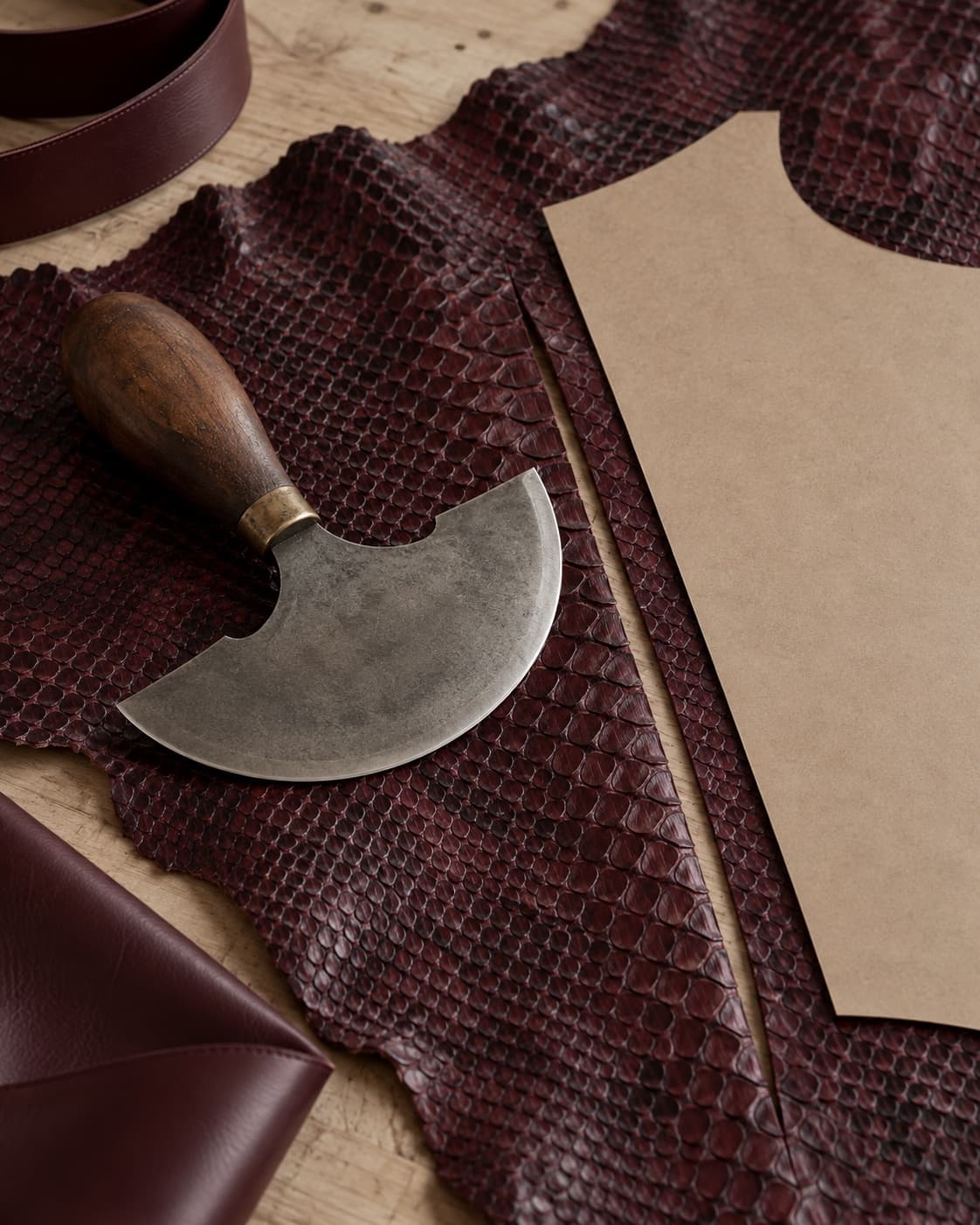 A leather knife and paper pattern piece resting on a python skin beside a clean cut line